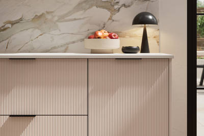 Fluted front kitchen Reed from Magnet in light neutral shade Shell, with a marbled splashback and black handles, herringbone wood flooring.