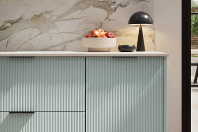 Fluted front kitchen Reed from Magnet in bright blue shade Sky, with a marbled splashback and black handles, herringbone wood flooring.