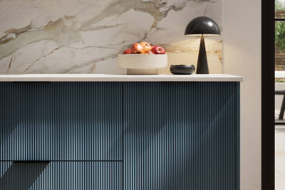 Fluted front kitchen Reed from Magnet in dark blue shade Voyage Blue, with a marbled splashback and black handles, herringbone wood flooring.