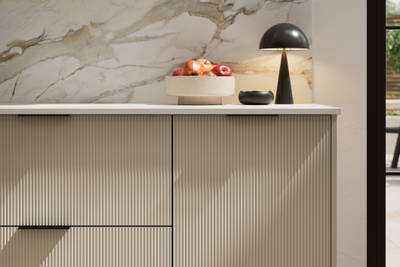 Fluted front kitchen Reed from Magnet in light neutral shade Parchment, with a marbled splashback and black handles, herringbone wood flooring.