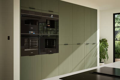Green fluted kitchen fronts on tall cabinets with built-in appliances and black handles.