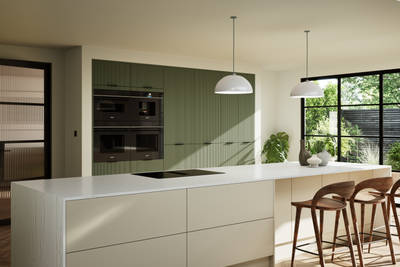 Green fluted kitchen fronts on tall cabinets with built-in appliances and black handles, light neutral shade kitchen island with white worktop and wooden barstools.