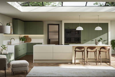 Green fluted kitchen fronts on tall cabinets with built-in appliances and black handles, light neutral shade kitchen island with white worktop and wooden barstools.