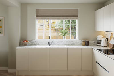 Open plan light neutral shade fluted kitchen with integrated appliances, white and grey marble worktop and upstand. Herringbone wood flooring.