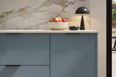 Fluted front kitchen Reed from Magnet in bright blue shade Portland Blue, with a marbled splashback and black handles, herringbone wood flooring.