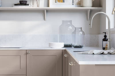 Ludlow, a traditional Shaker-style premium feel kitchen range with a visible woodgrain on its panelled doors here shown in the shade Cornish Clay styled with steel knobs, steel tap, a white marbled worktop with matching splashback.