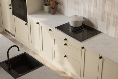 View from above of contemporary Shaker kitchen Ambleside from Magnet in neutral shade Sand with black sink and tap in kitchen island, induction hob with extractor, marbled worktop and black knobs.