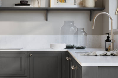 Bewdley Charcoals painted wood grain Shaker kitchen cabinetry with steel knobs, steel tap, white marbled worktop and matching backsplash, an open shelf on the wall above cabinets with ceramics and a vase of flowers.