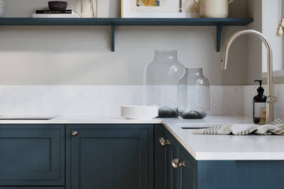 Bewdley Midnight painted wood grain Shaker kitchen cabinetry with steel knobs, steel tap, white marbled worktop and matching backsplash, an open shelf on the wall above cabinets with ceramics and a vase of flowers.
