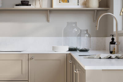 Bewdley Shell painted wood grain Shaker kitchen cabinetry with steel knobs, steel tap, white marbled worktop and matching backsplash, an open shelf on the wall above cabinets with ceramics and a vase of flowers.