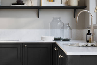 Bewdley Sumi Black painted wood grain Shaker kitchen cabinetry with steel knobs, steel tap, white marbled worktop and matching backsplash, an open shelf on the wall above cabinets with ceramics and a vase of flowers.