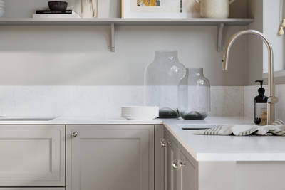 Bewdley Dove Grey painted wood grain Shaker kitchen cabinetry with steel knobs, steel tap, white marbled worktop and matching backsplash, an open shelf on the wall above cabinets with ceramics and a vase of flowers.