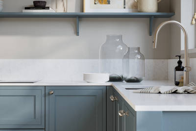 Bewdley Portland Blue painted wood grain Shaker kitchen cabinetry with steel knobs, steel tap, white marbled worktop and matching backsplash, an open shelf on the wall above cabinets with ceramics and a vase of flowers.