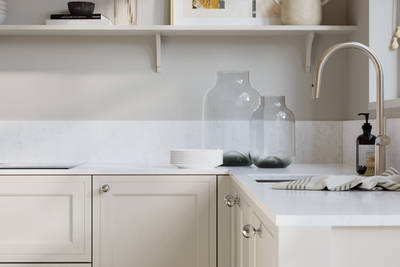 Bewdley Fresh Linen painted wood grain Shaker kitchen cabinetry with steel knobs, steel tap, white marbled worktop and matching backsplash, an open shelf on the wall above cabinets with ceramics and a vase of flowers.