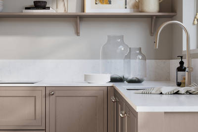 Bewdley Cornish Clay painted wood grain Shaker kitchen cabinetry with steel knobs, steel tap, white marbled worktop and matching backsplash, an open shelf on the wall above cabinets with ceramics and a vase of flowers.