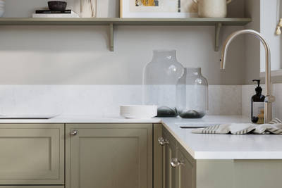 Bewdley French Clay painted wood grain Shaker kitchen cabinetry with steel knobs, steel tap, white marbled worktop and matching backsplash, an open shelf on the wall above cabinets with ceramics and a vase of flowers.