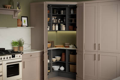 Opened walk-in pantry in Shaker style painted wood grain Bewdley kitchen in neutral shade Cornish Clay, tall cabinets with marbled worktop and matching backsplash and gas range cooker.