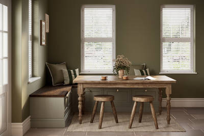 Dining area with low Shaker style painted wood grain cabinets Bewdley cabinets as a bench with a wooden table and stools in a room with painted green walls.