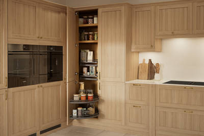 Traditional premium contemporary Shaker kitchen Ambleside in oak with brass knobs and handles, built-in ovens in tall cabinetry, opened tall corner cabinet with oak shelves and pull-out carousel.