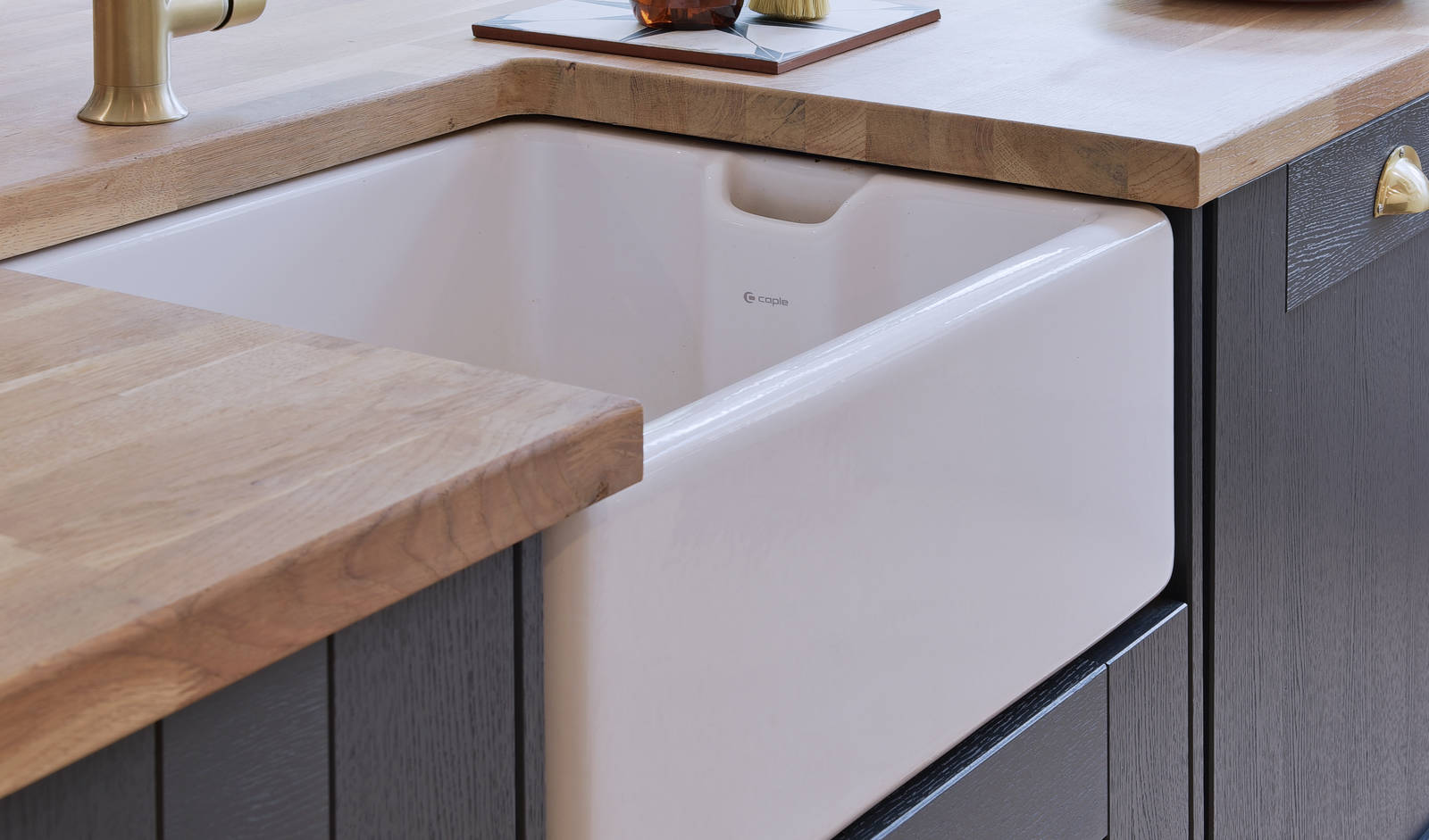Close-up of Caple Belfast Ceramic sink which adds a rustic charm to the kitchen island. Paired with a wood worktop and brass tap.