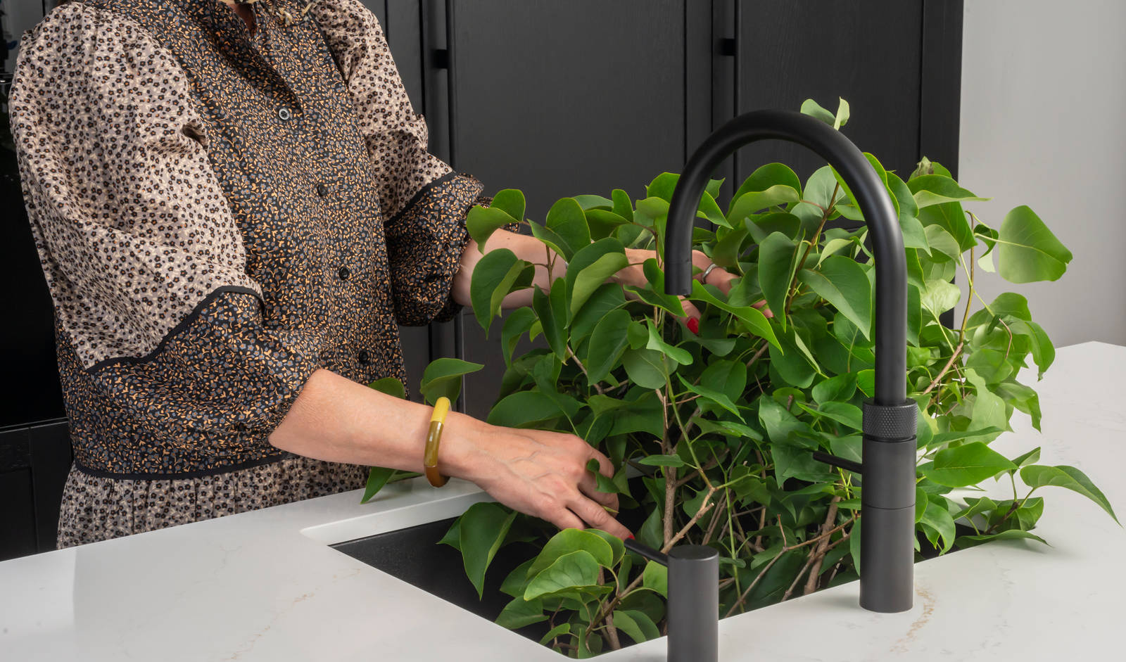 Et nydelig svart kjøkken i lun eik med kjøkkenøy dekket av lys komposittstein og stilige matt-svarte håndtak.