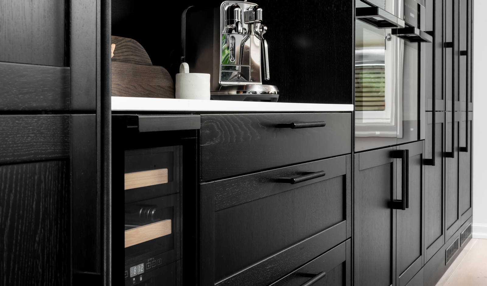 Et nydelig svart kjøkken i lun eik med kjøkkenøy dekket av lys komposittstein og stilige matt-svarte håndtak.