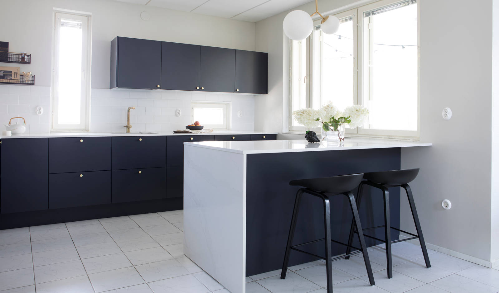 Tummansininen Meri maalattu sileä keittiö, jossa valkoinen marmoroitu työtaso ja siihen sopiva roiske, keittiösaareke istuinalueella, messinkinupit ja messinkihana