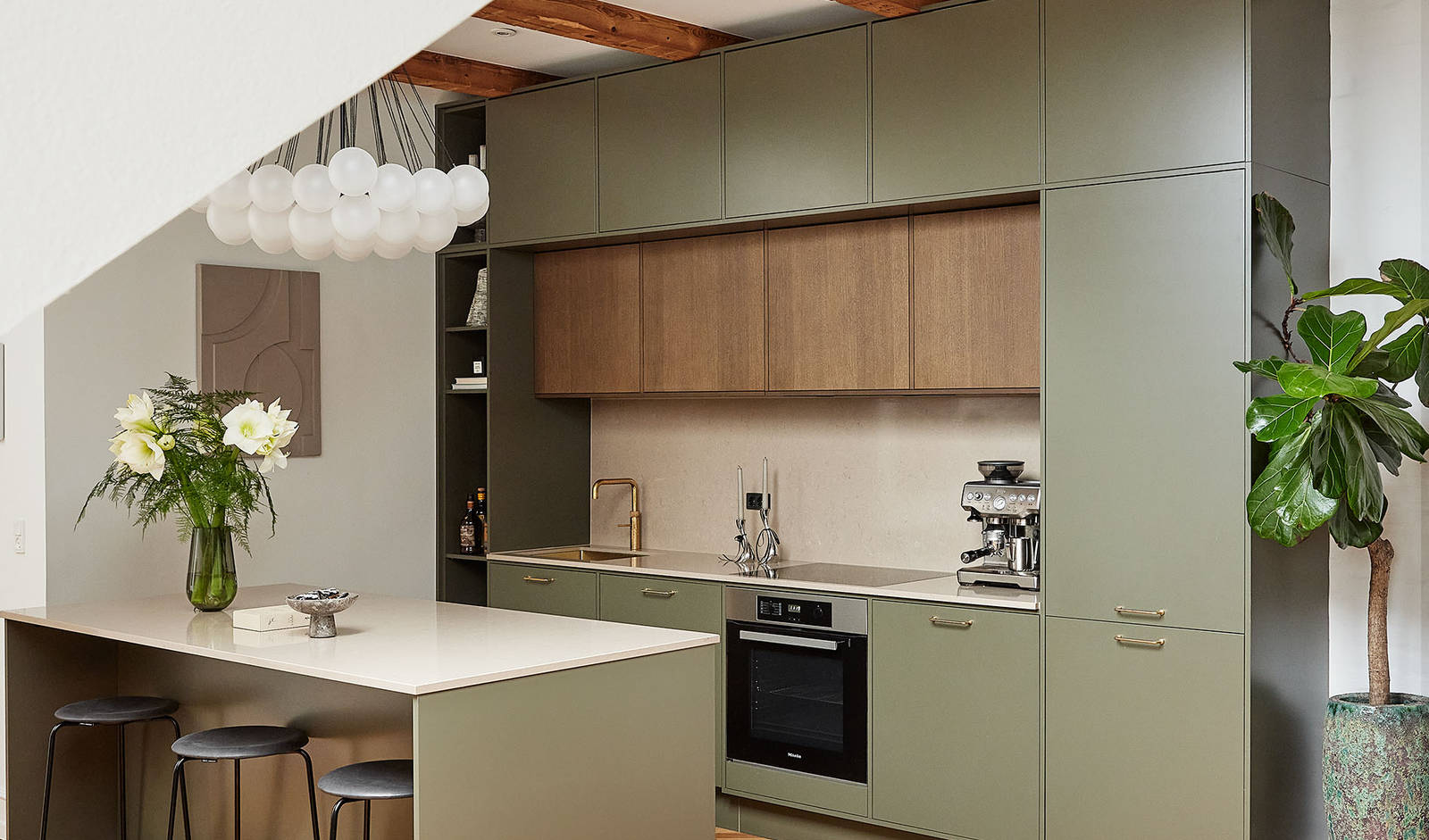 Athena-køkkenet fra INVITA med køkkenøy i den grønne farve Oliven, og det mørke træ på overskabene matcher de mørke træbjælker.