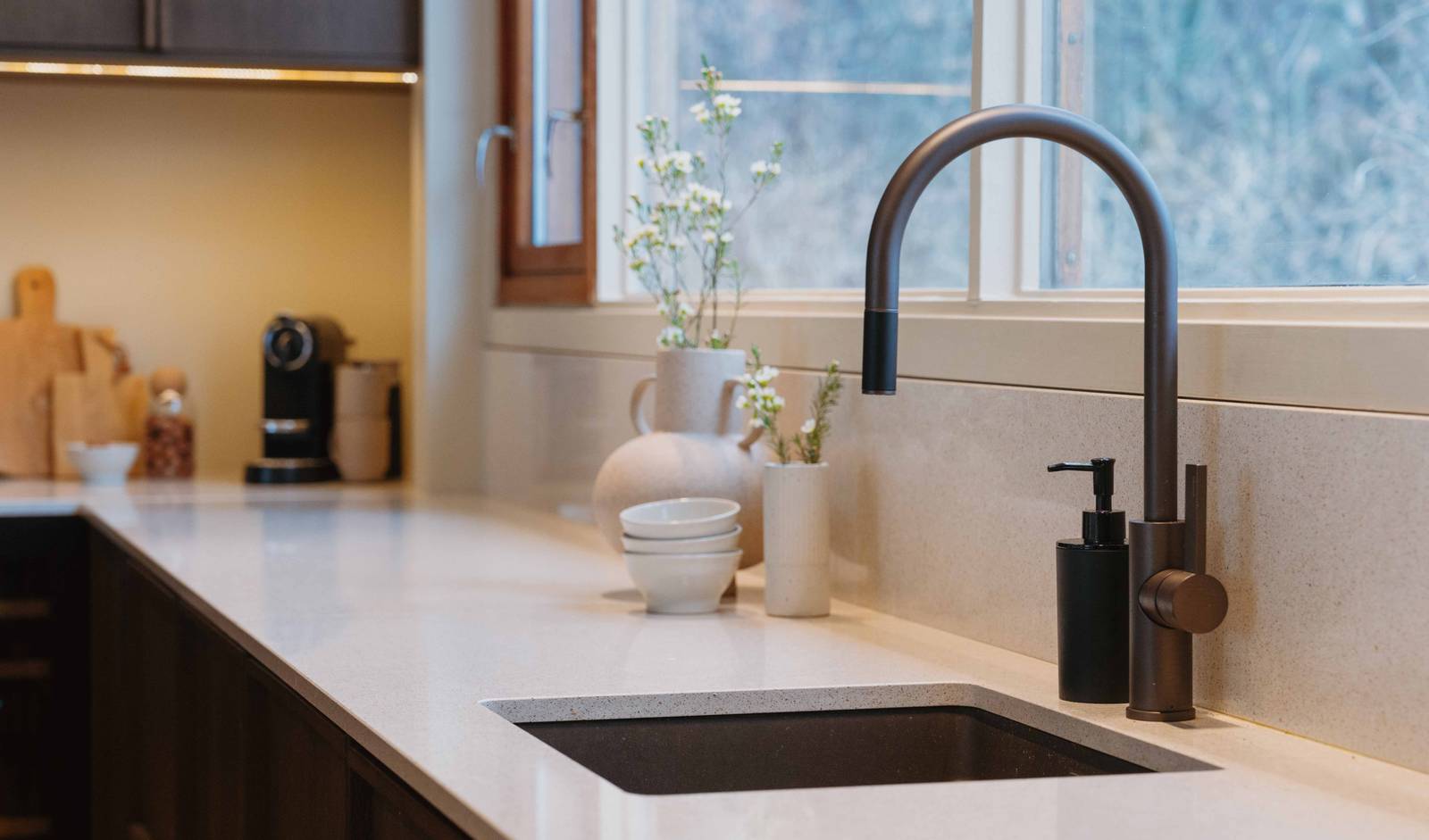 Nærbilde av sort vask og sort blandebatteri i eikekjøkkenet Favn fra Sigdal i beisfargen Nøtt med matchende tre håndtag og benkeplate Blanco City fra Silestone.