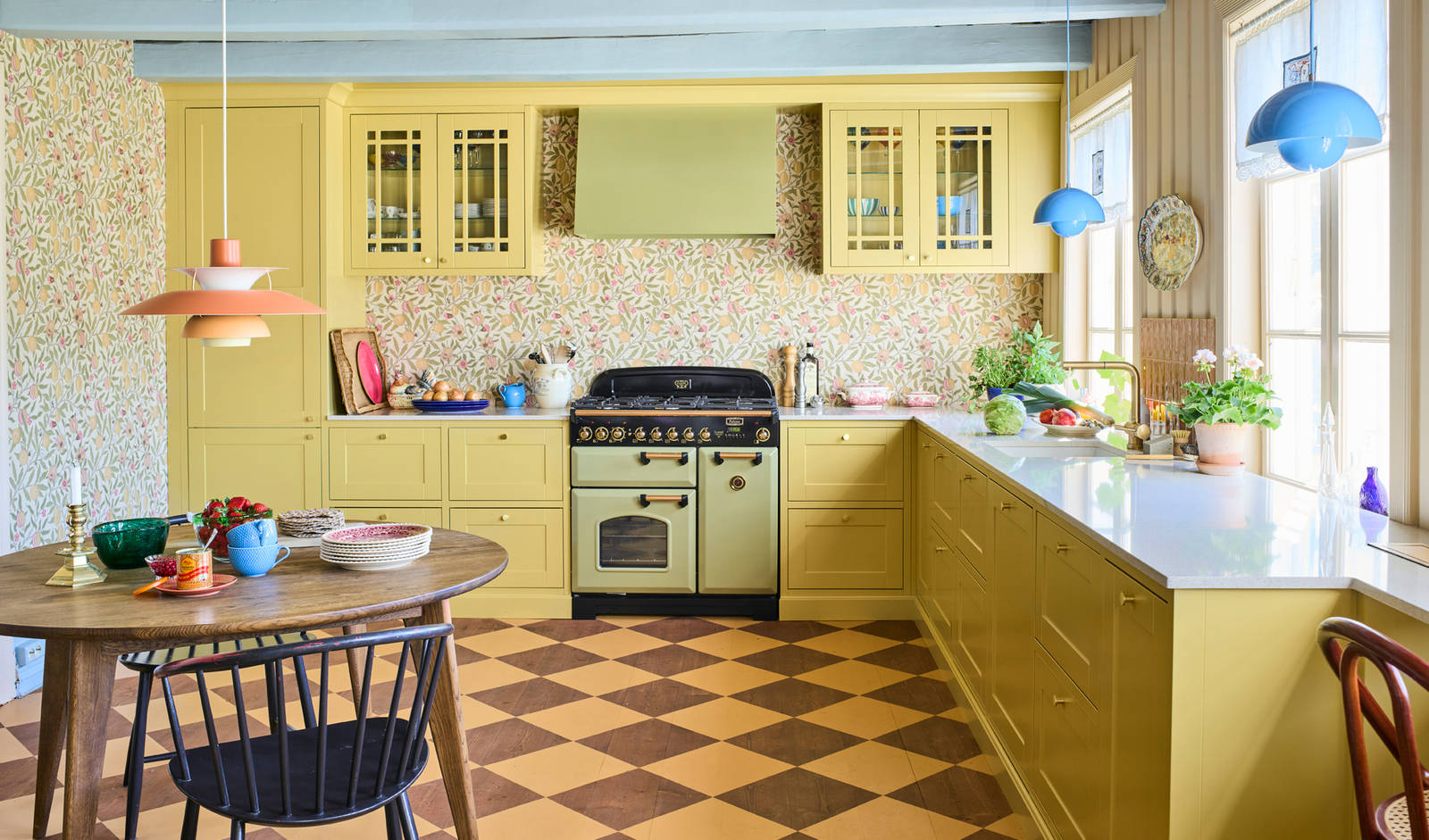 Landlig rammekjøkken Scala Inframe fra Sigdal som gir en snekkerbygged preg, vitrineskaber, Falcon Classic Olive green komfyr med gassbrennere og Røroshetta Grue ventilator i samma fargekode, rutete gulv