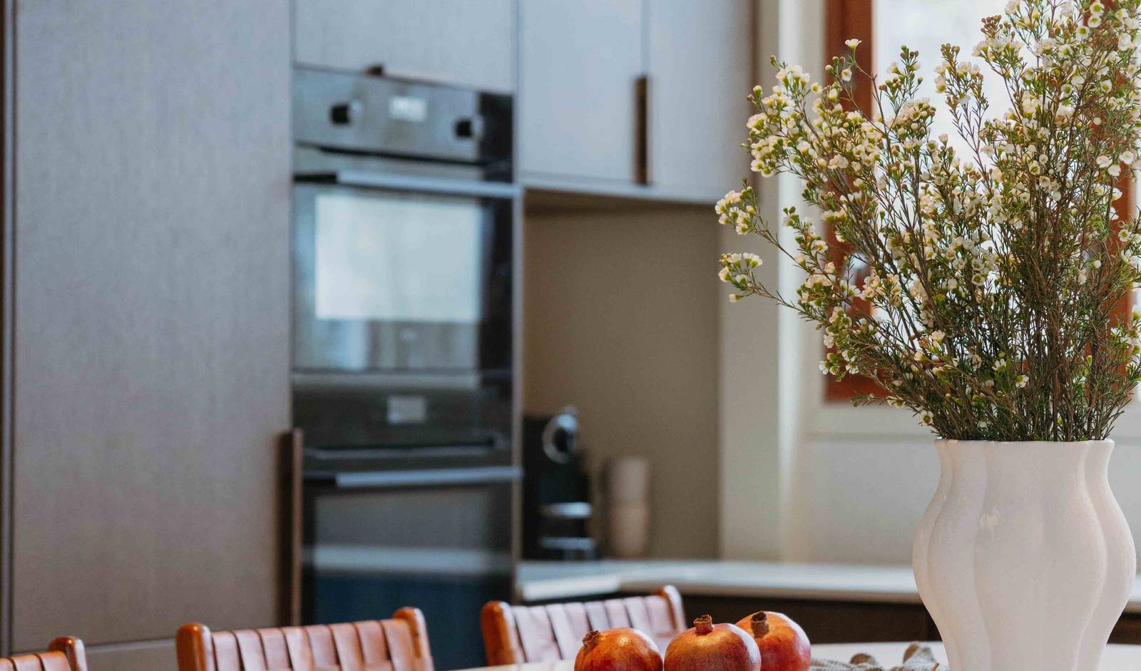 Et skærebræt med granatæbler og en vase på køkkenøen i Forever Oak køkkenet fra Invita