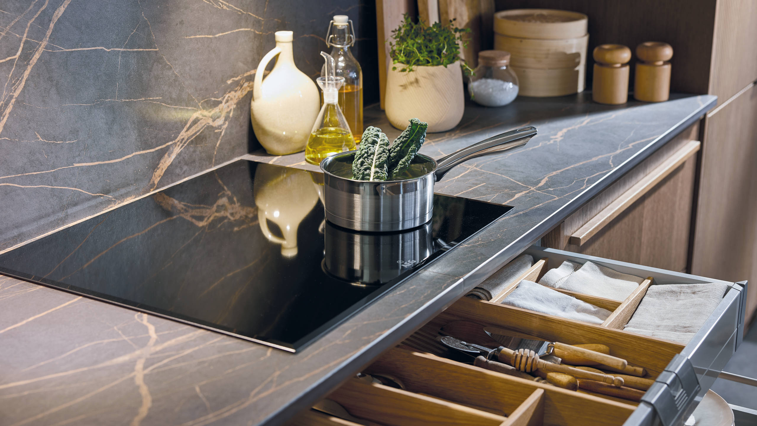 Induction hob on marbled worktop, matching backsplash, and an opened drawer with oak inserts