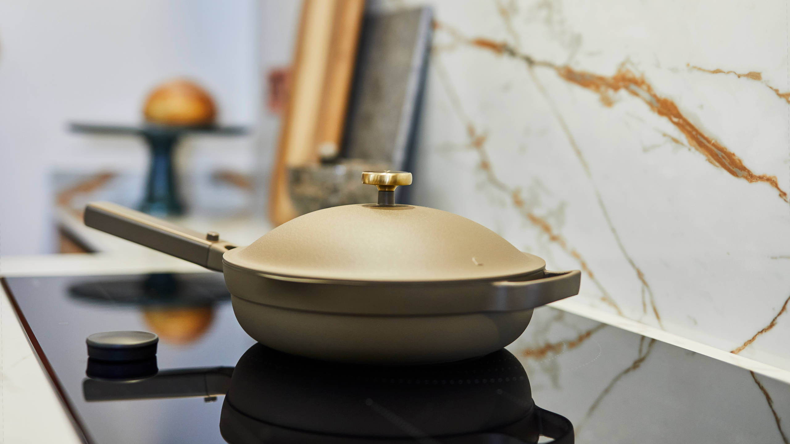 A green pan with a lid on top of a black glass kitchen hob.
