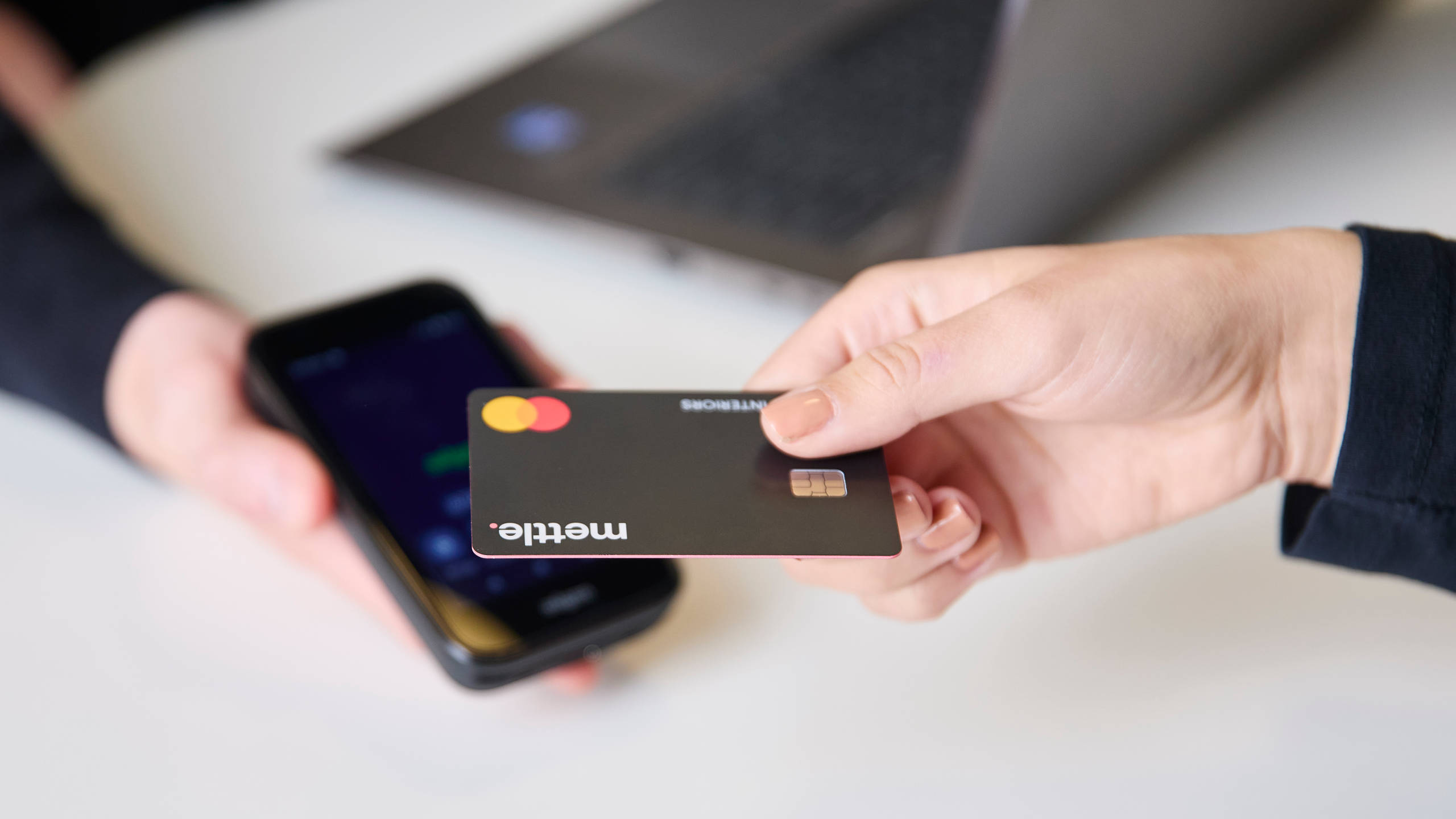 Close-up of hand holding a credit card  over a smartphone held by another person for payment at Magnet store