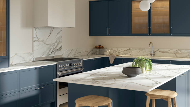 View over kitchen island breakfast bar in modern Shaker kitchen Brunswick Voyage blue with white and grey marbled worktop and matching splashback, and vitrine cabinets with fluted glass.