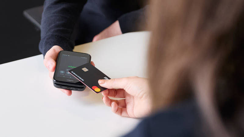 Close-up of customer holding a credit card over a smartphone held by Magnet colleague for payment at Magnet store