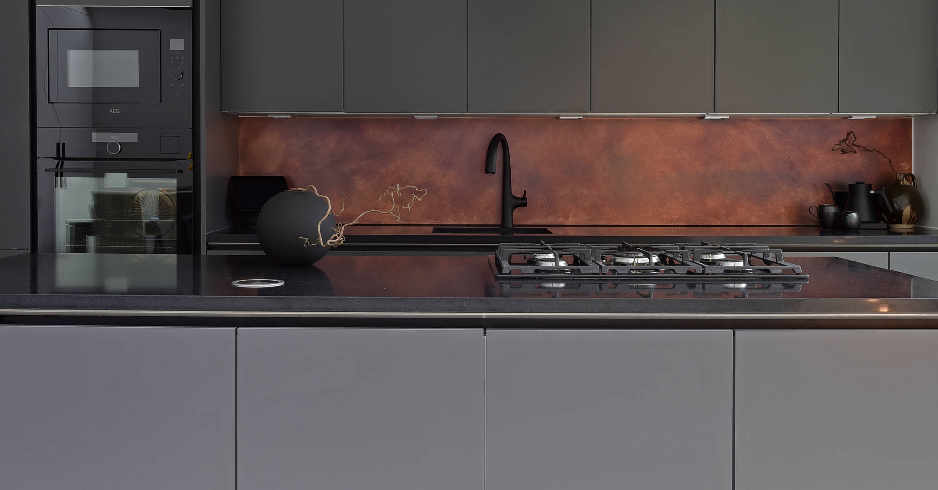 View of kitchen island with black granite worktop, gas hob and Elica HD seashell hood in black in the ultra-contemporary integra soho charcoals