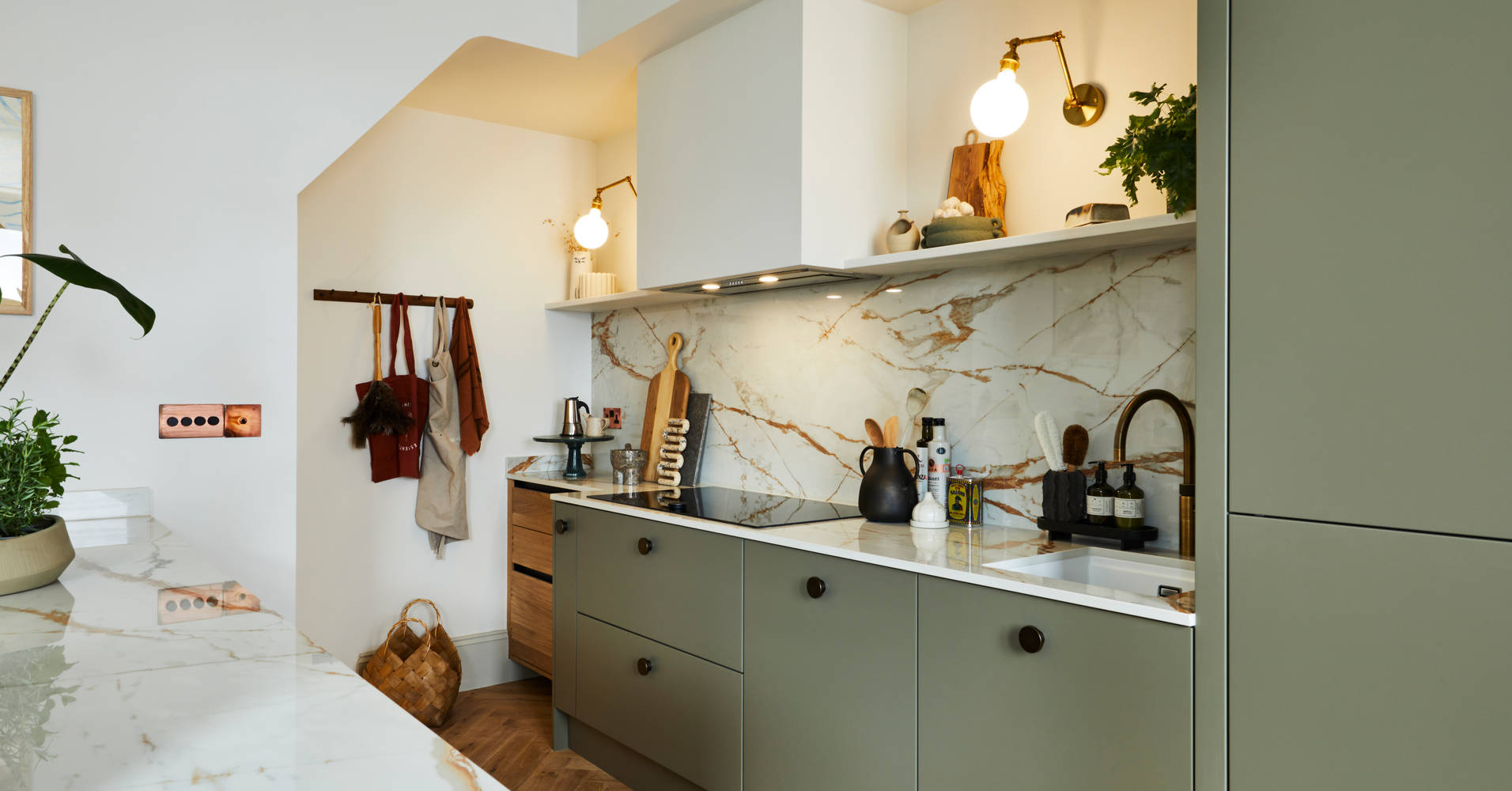 Modern slab Soho Balmoral cabinet paired with modern appliances, a marbled worktop and backsplash, brass details and plants.