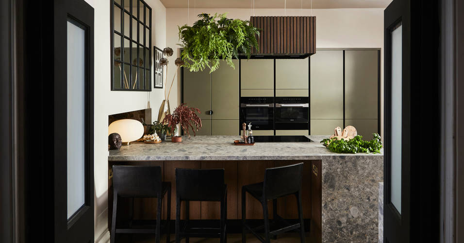 View through opened dark wood doors of the biophilic Dramatic neutral Balmoral Soho and Nordic Nature kitchen from Magnet and matching dark chairs by the bar area of the kitchen island.