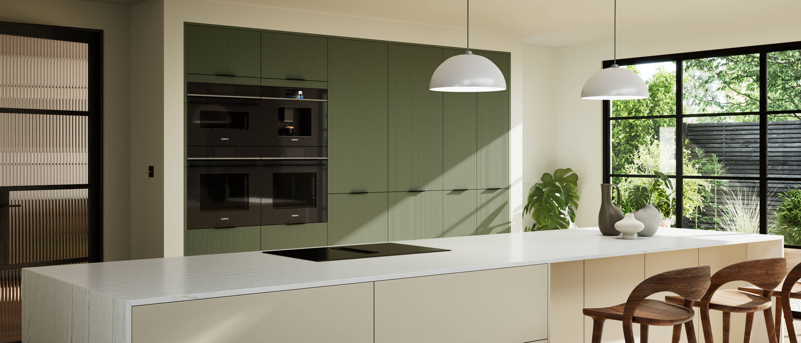 Green fluted kitchen fronts on tall cabinets with built-in appliances and black handles, light neutral shade kitchen island with white worktop and wooden barstools.
