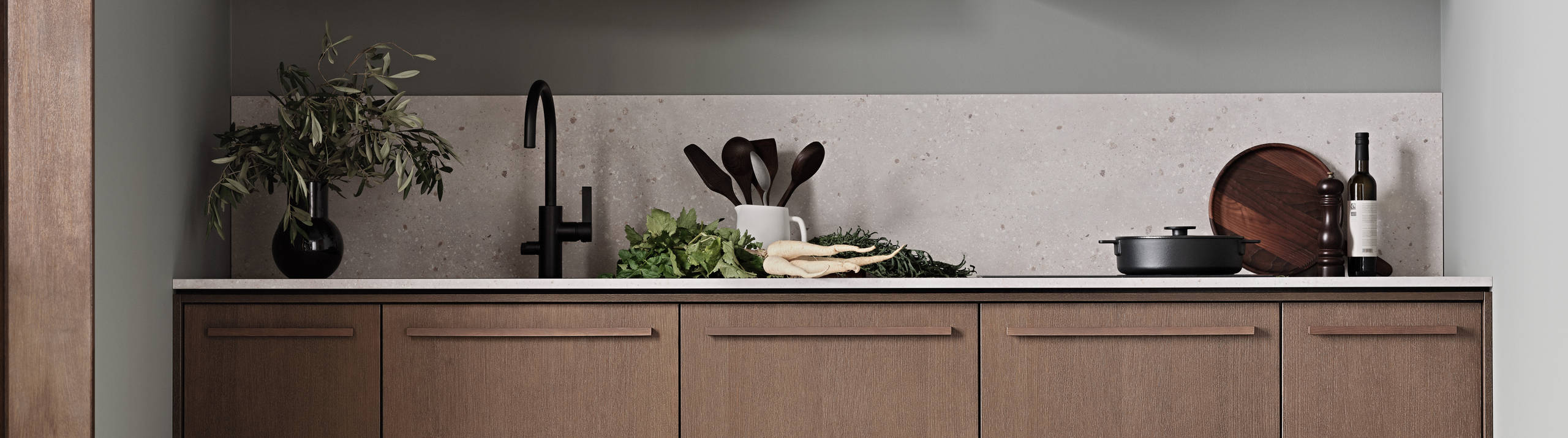 Køkken Forever Oak fra INVITA, mørk eg køkkenskabe med massiv tre mørk eg håndtag, komposit bordplade, sort armatur og vitrineskab med riflede glas i tynd, sort aluminiumsramme