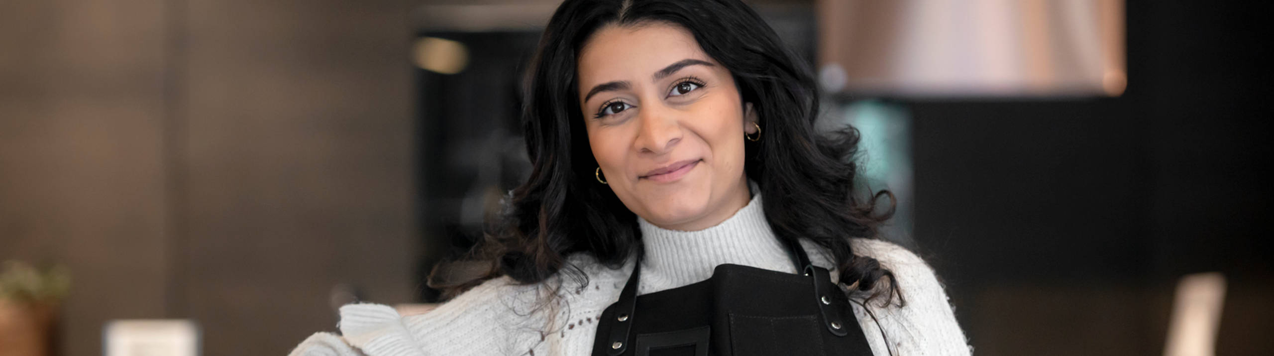 Kjøkkendesigner i hvit skjorte og blått forkle smiler til kameraet utenfor Sigdals butikk