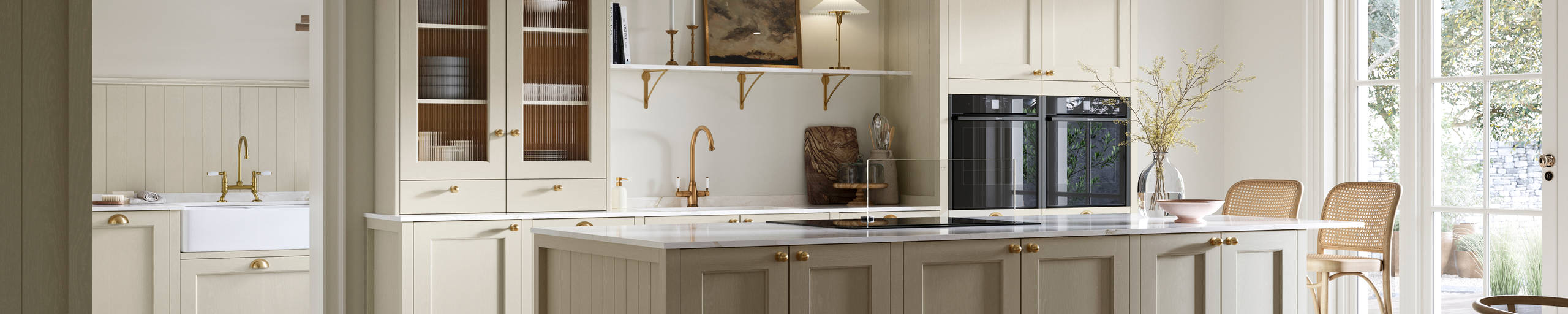 Open plan living room and Traditional Shaker-style kitchen Ludlow Parchment with tactile woodgrain, flute glass vitrine cabinets,  brass acessories like handles and tap, integrated ovens, a kitchen island and light wood herringbone flooring.