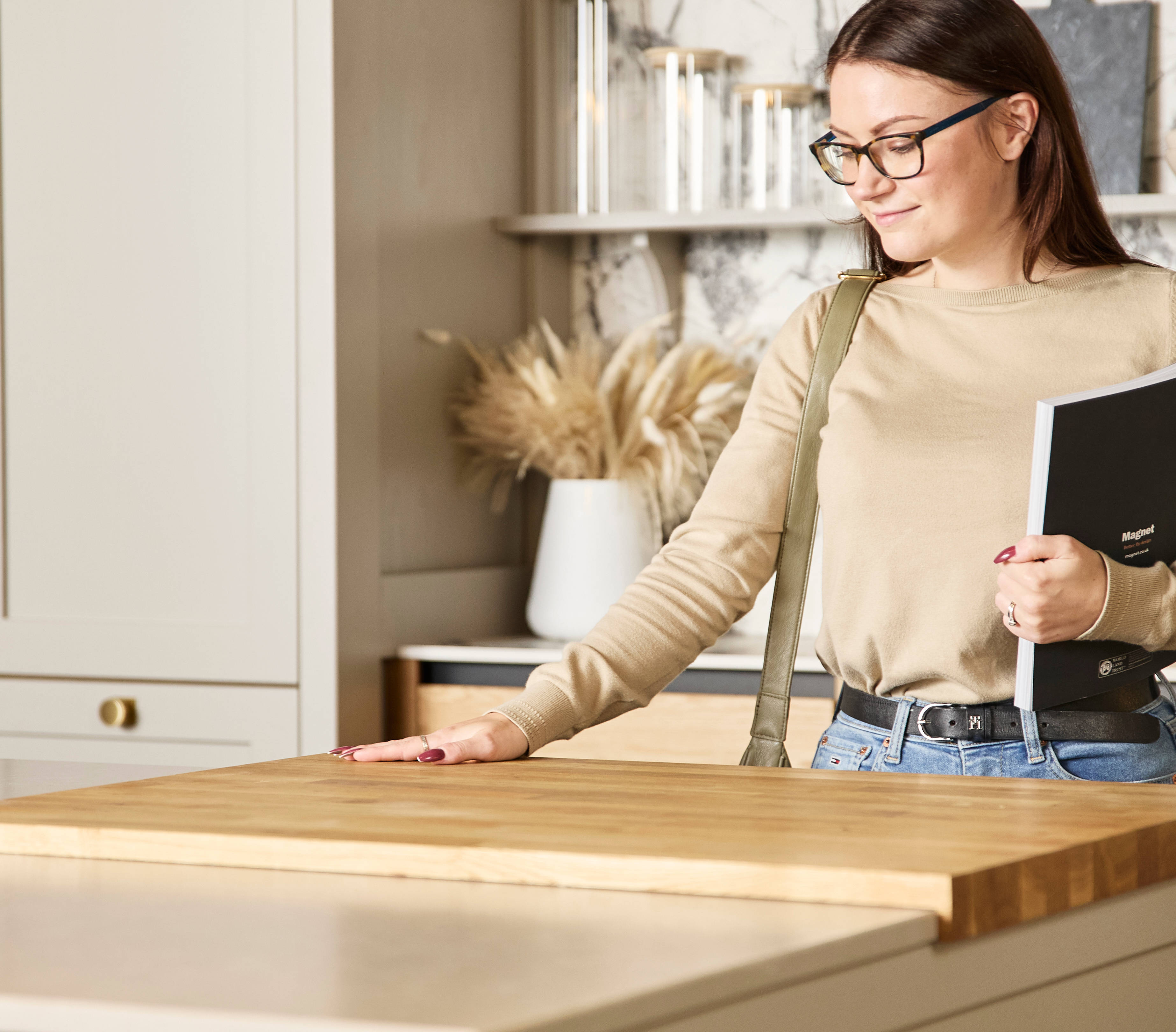 Woman holding a brochure feeling the wood worktop with her hand in a neutral shade Shaker style kitchen in a Magnet Showroom