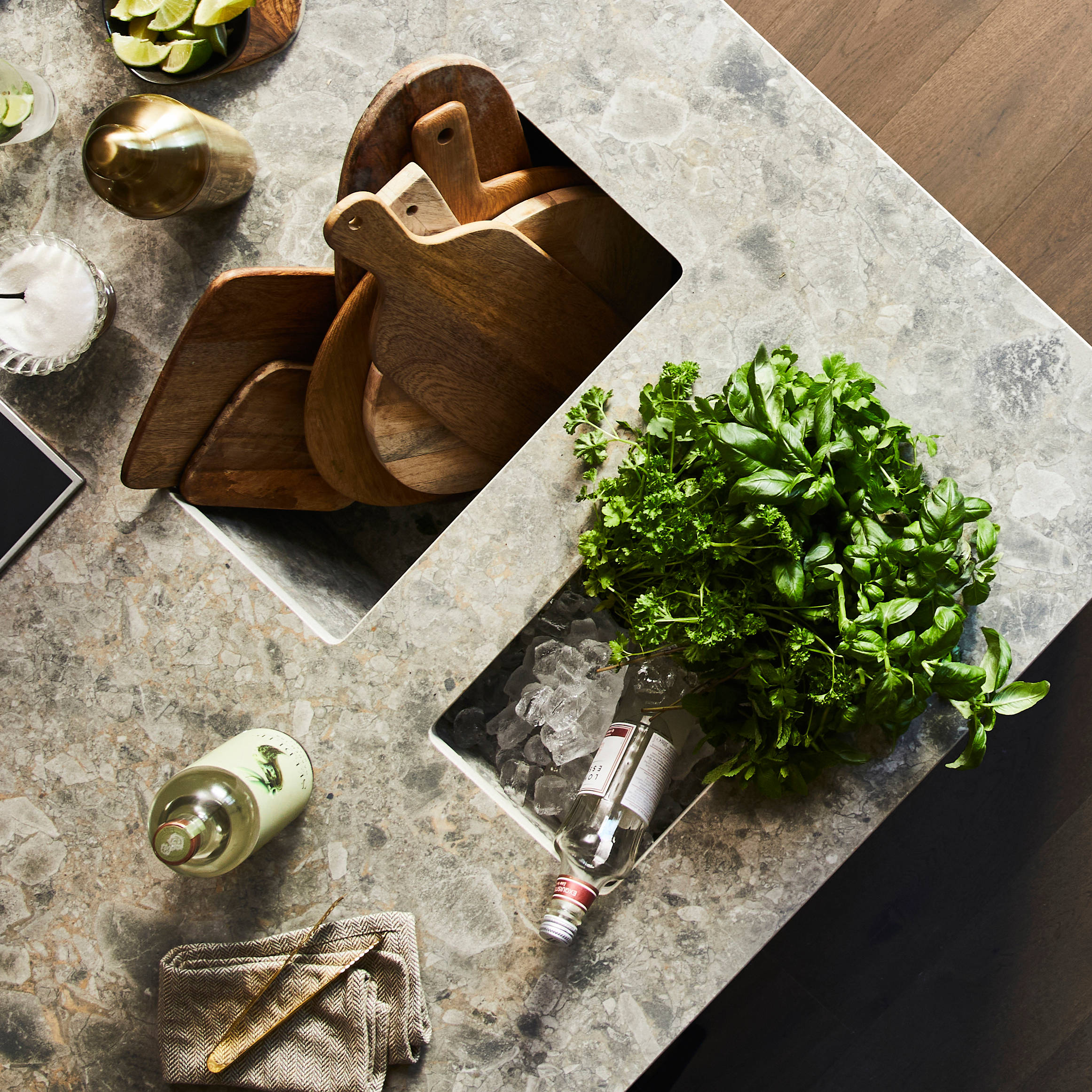 Birds eye view of kitchen island with Dekton in Ceppo worktop,wooden cutting boards with cut up lime fruits and a large plant of basil.