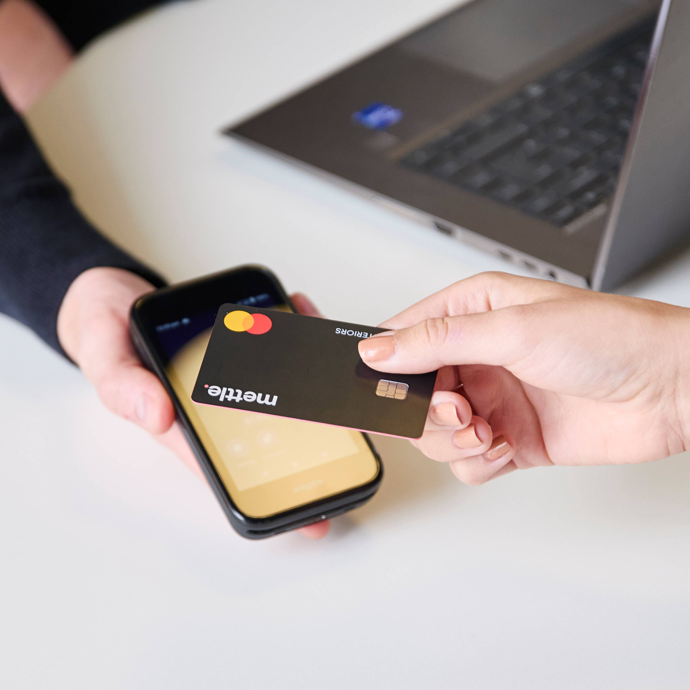 Close-up of hand holding a credit card  over a smartphone held by Magnet colleague for payment at Magnet store
