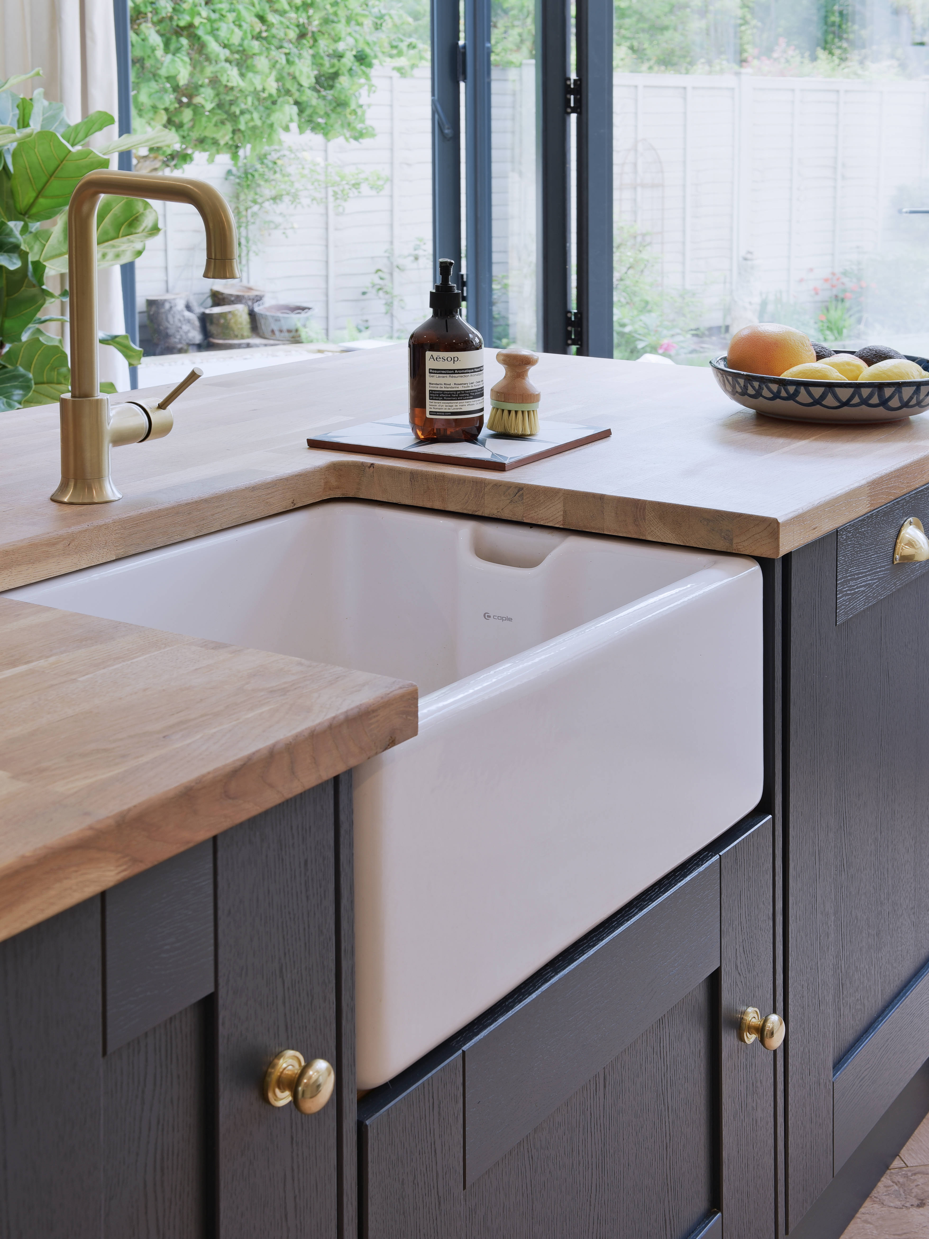 Close-up of Caple Belfast Ceramic sink which adds a rustic charm to the kitchen island. Paired with a wood worktop and brass tap.