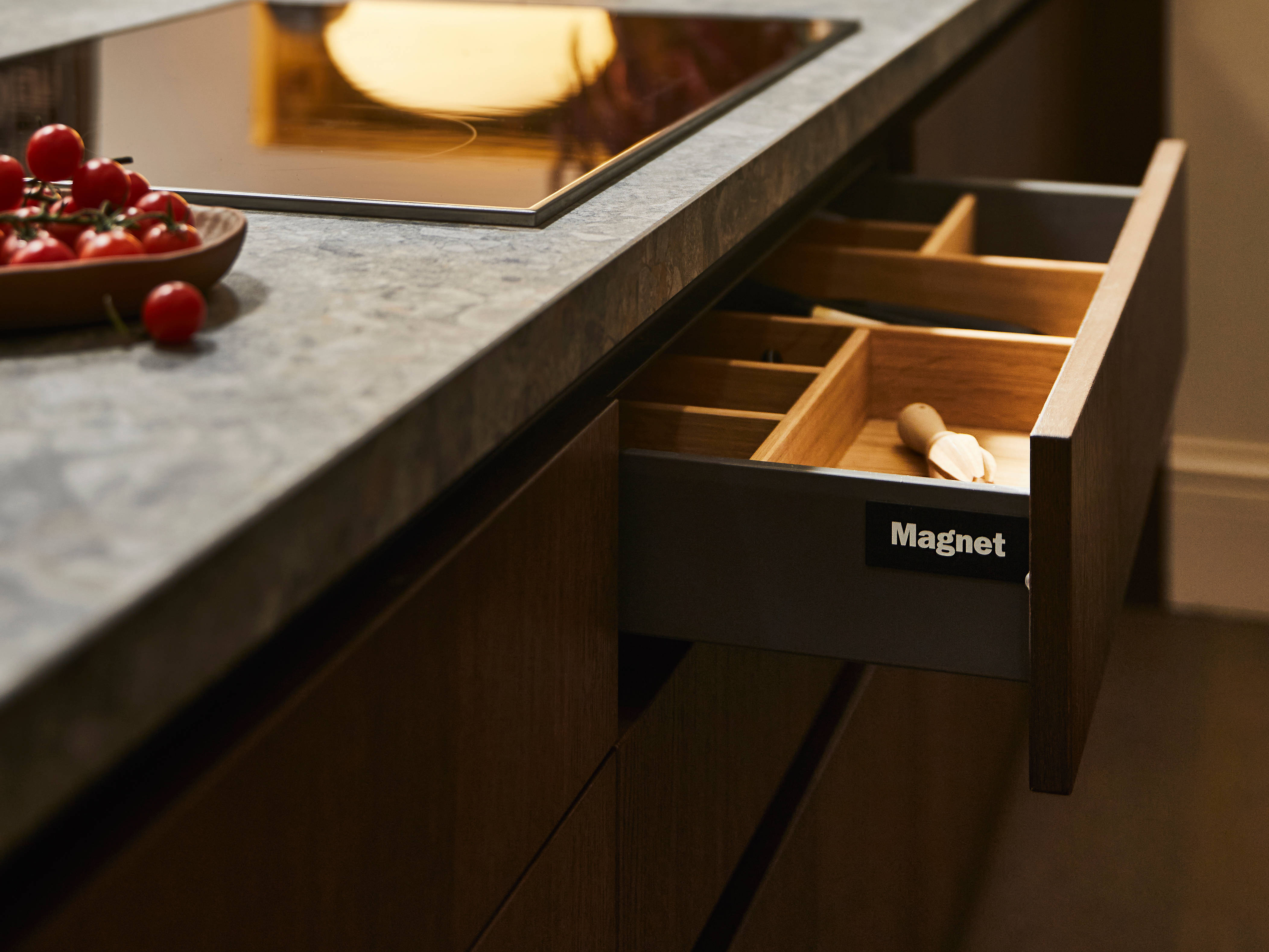 View of kitchen island with an opened Nordic Nature drawer containing oak inserts, a Dekton in Ceppo worktop and potted plants in background.