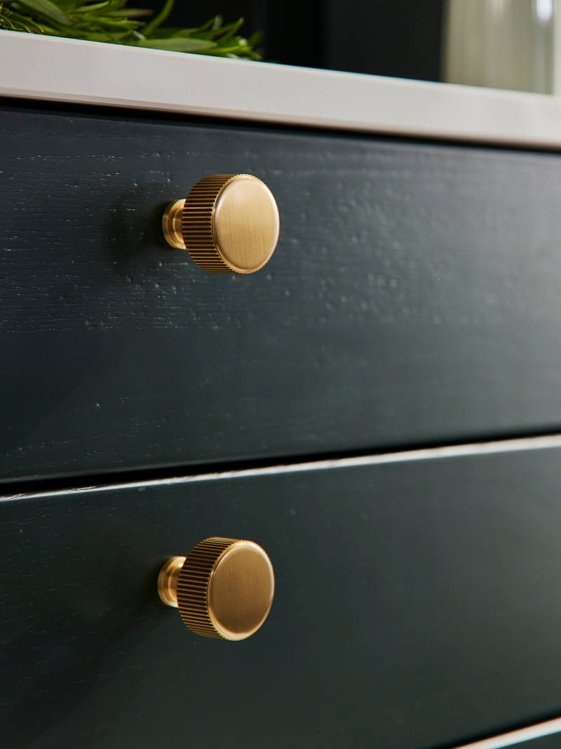 Close-up view of dark green Ludlow kitchen with brass knobs