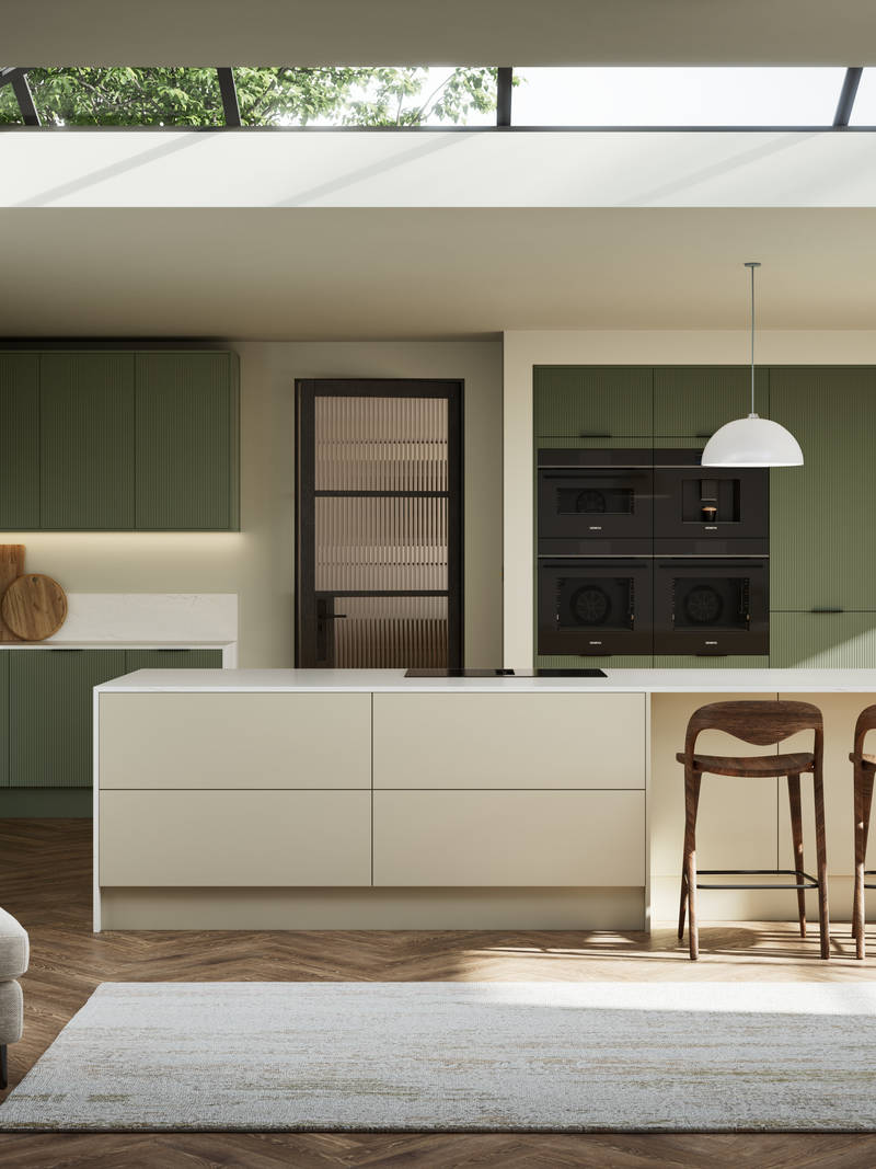 Green fluted kitchen fronts on tall cabinets with built-in appliances and black handles, light neutral shade kitchen island with white worktop and wooden barstools.